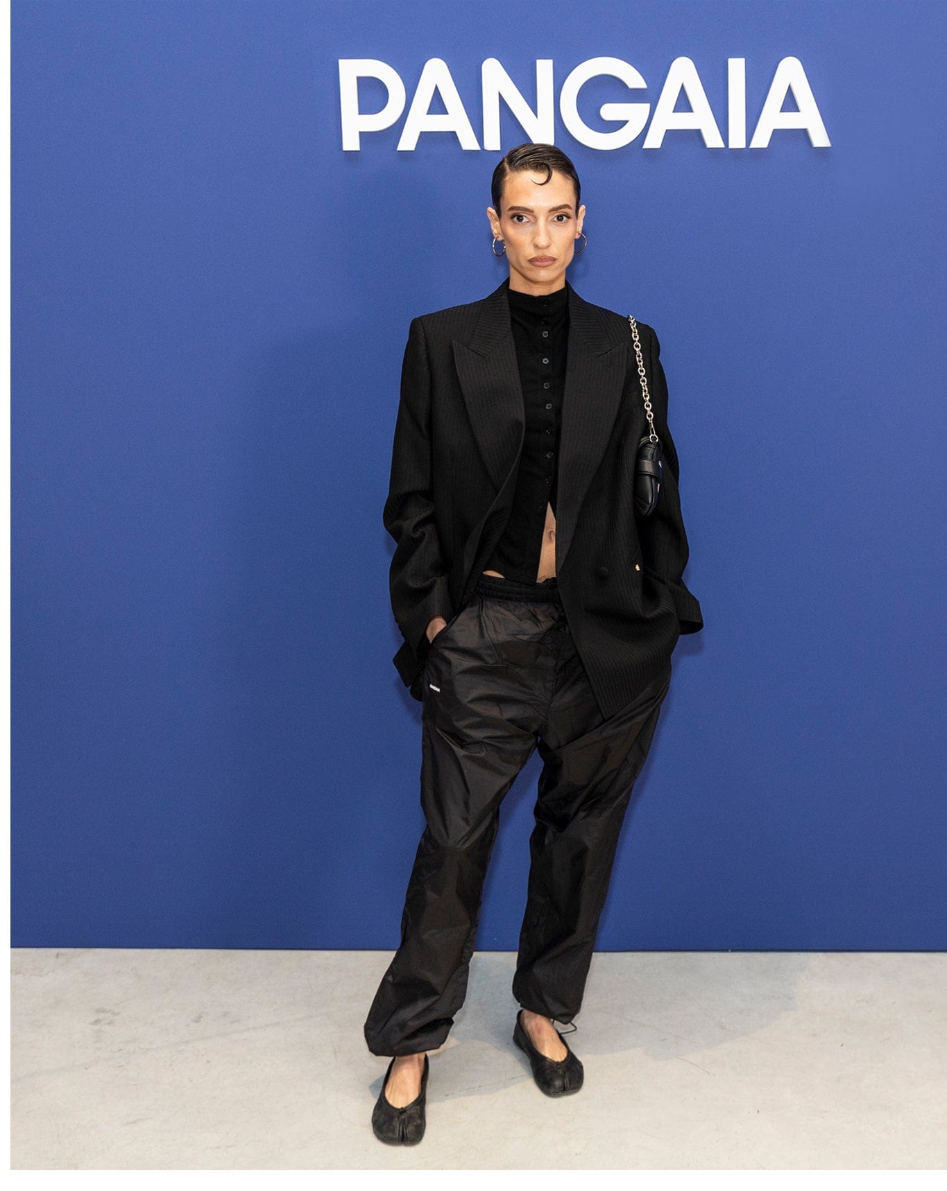 Black oversized pinstripe blazer, black cropped button-front top, relaxed black nylon pants, and tabi flats on model