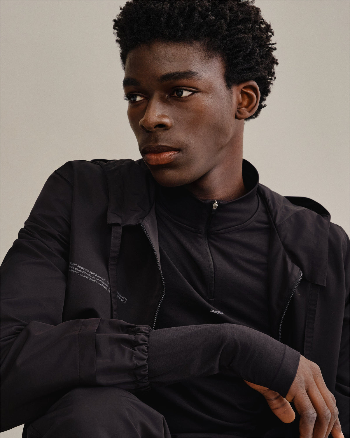 Pangaia men's black biobased nylon zip jacket with stand collar, elastic cuffs, layered over performance quarter-zip Athletic