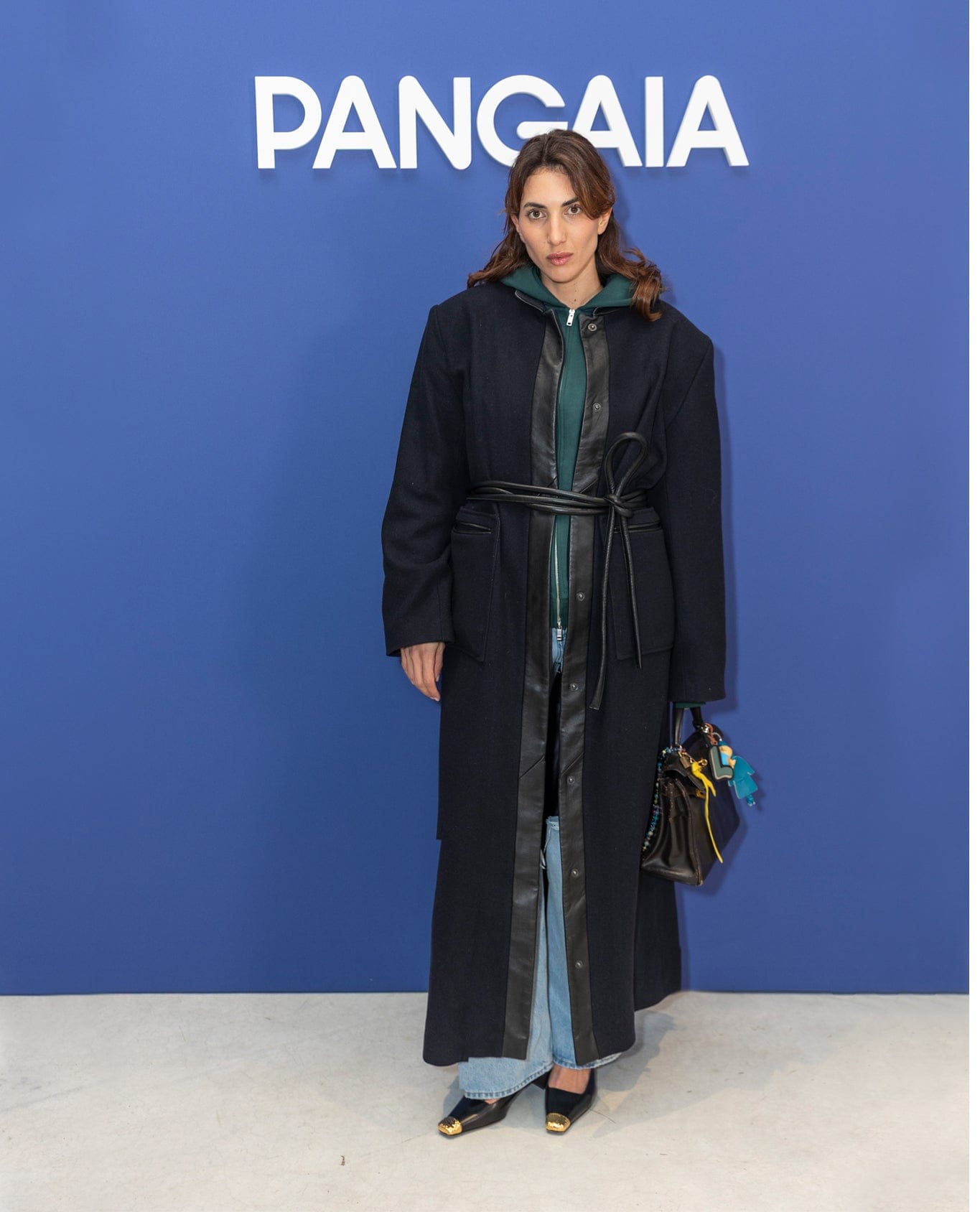 Oversized black wool blend long coat with faux leather trim and tie belt, green zip hoodie, light denim jeans