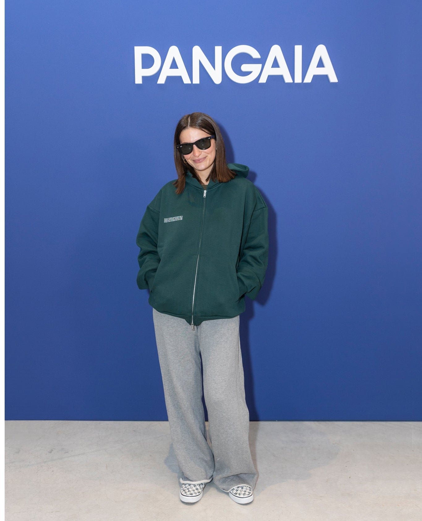 Woman wearing dark green oversized full-zip hoodie, heather grey wide-leg sweatpants, and patterned slip-on shoes