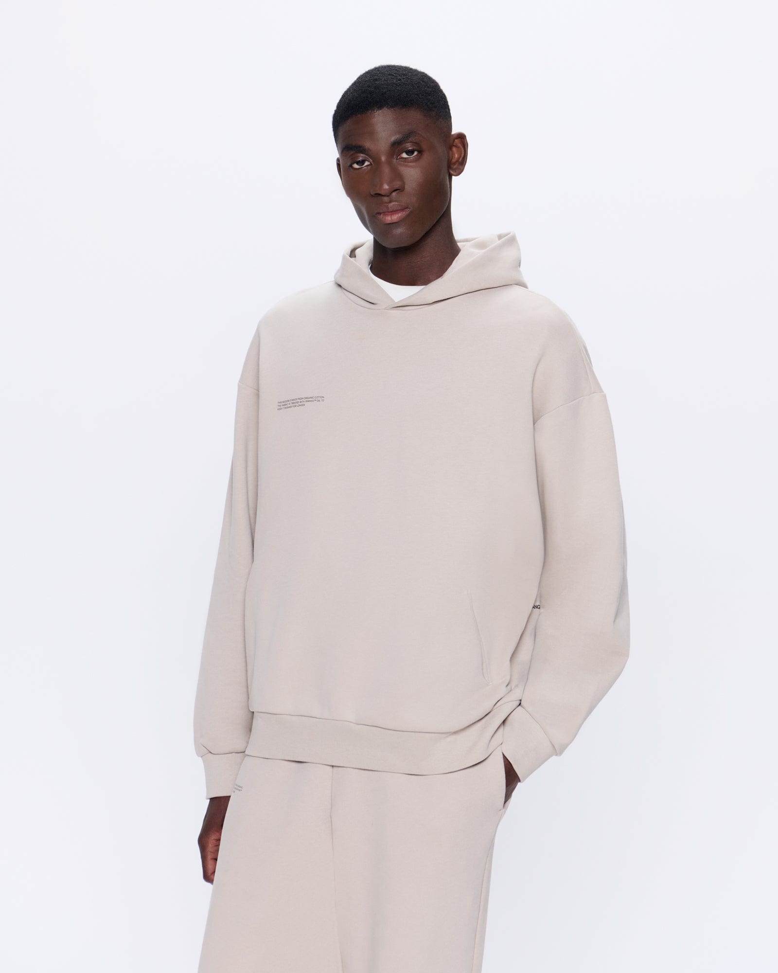 Model wearing an oversized sand beige heavyweight organic cotton hoodie with kangaroo pocket and matching sweatpants