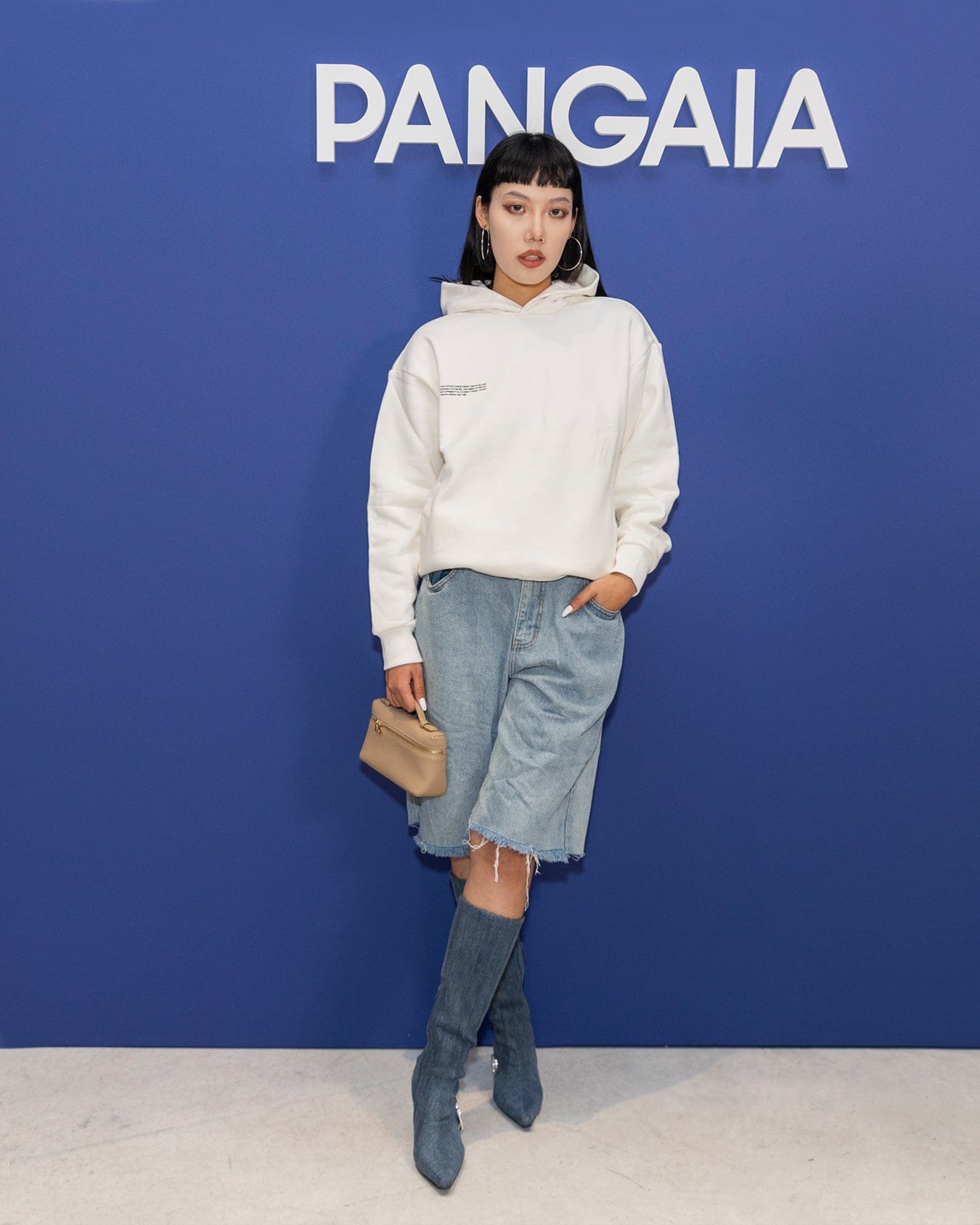 Woman wearing Pangaia white oversized hoodie, light wash denim Bermuda shorts, frayed hem, and denim over-the-knee boots