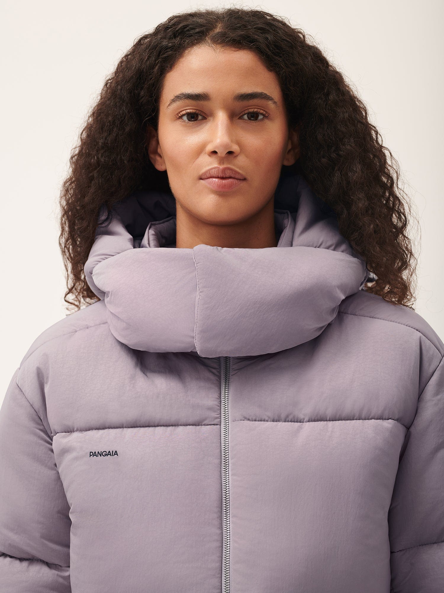 Female model in a relaxed-fit lavender purple quilted puffer jacket with a padded high collar and front zipper. Pangaia branding