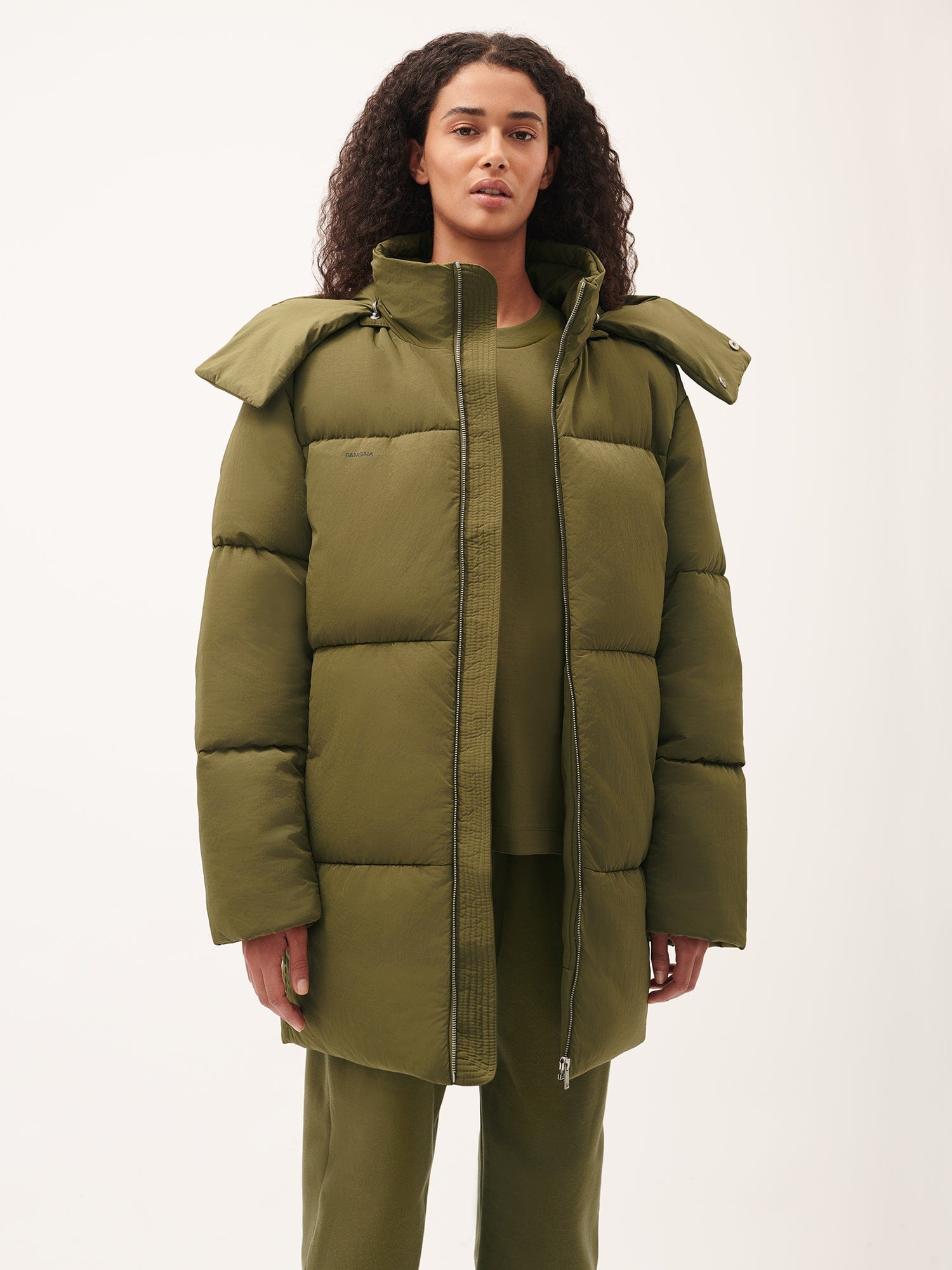Pangaia women's olive green oversized padded puffer jacket. Matte finish, mid-length, high collar, detachable hood