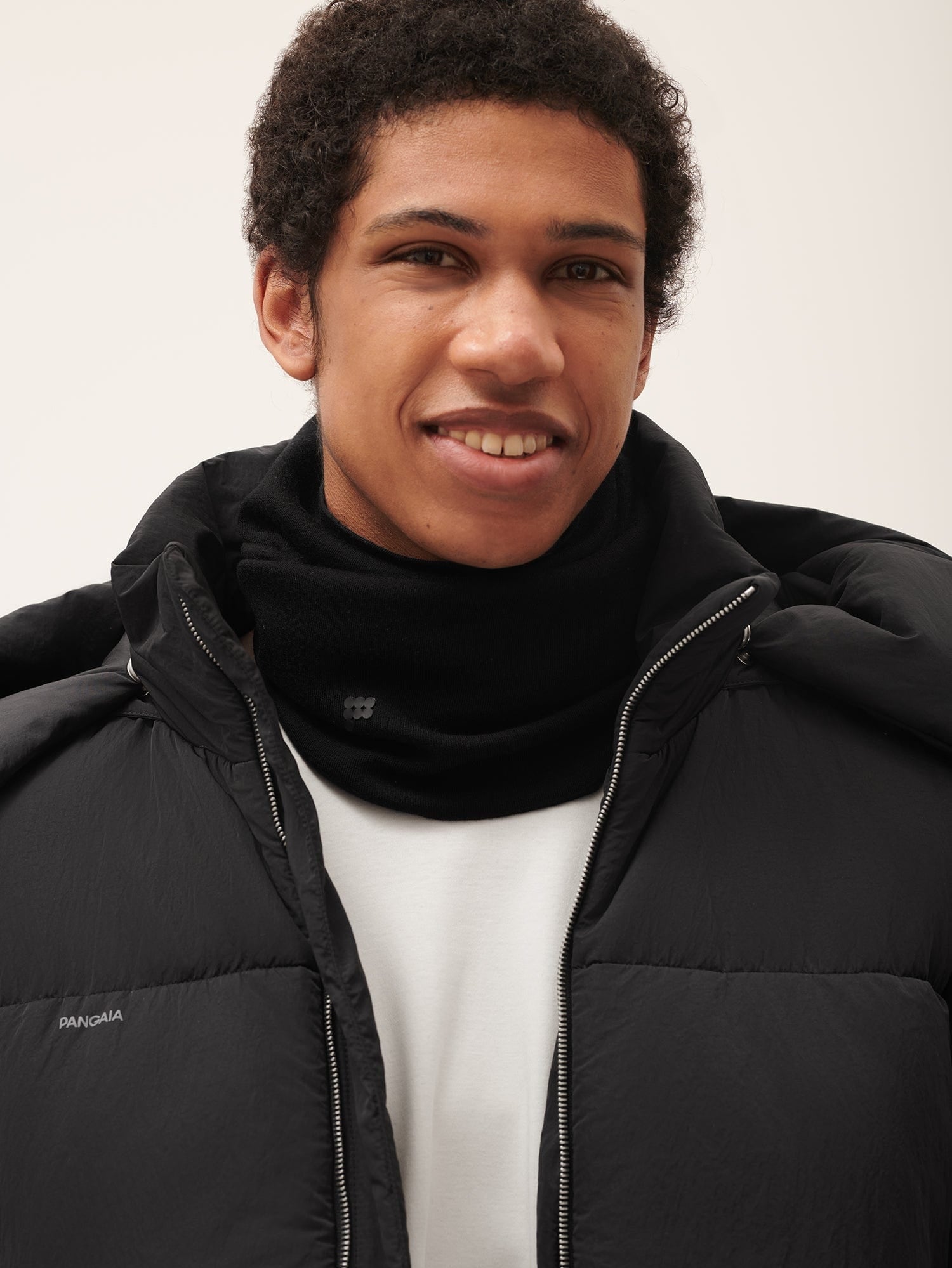 Black puffer jacket, black snood neck warmer, white t-shirt on male model, PANGAIA logo