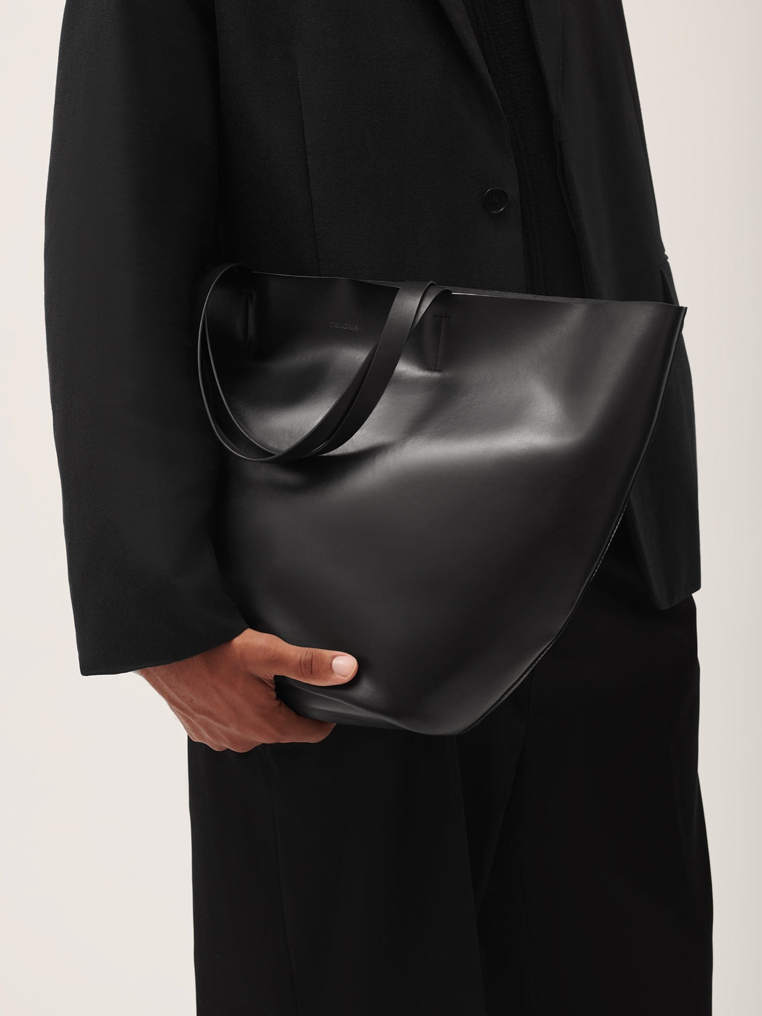 Black PANGIA smooth matte leather tote bag minimalist design carried by model wearing black blazer premium shoulder bag