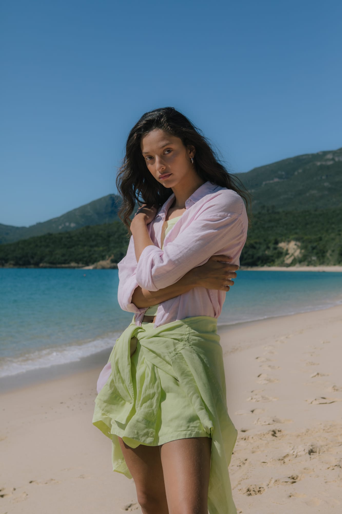 Female model wearing light pink linen button-up shirt, lime green crop top, and lime green resort shorts tied at waist
