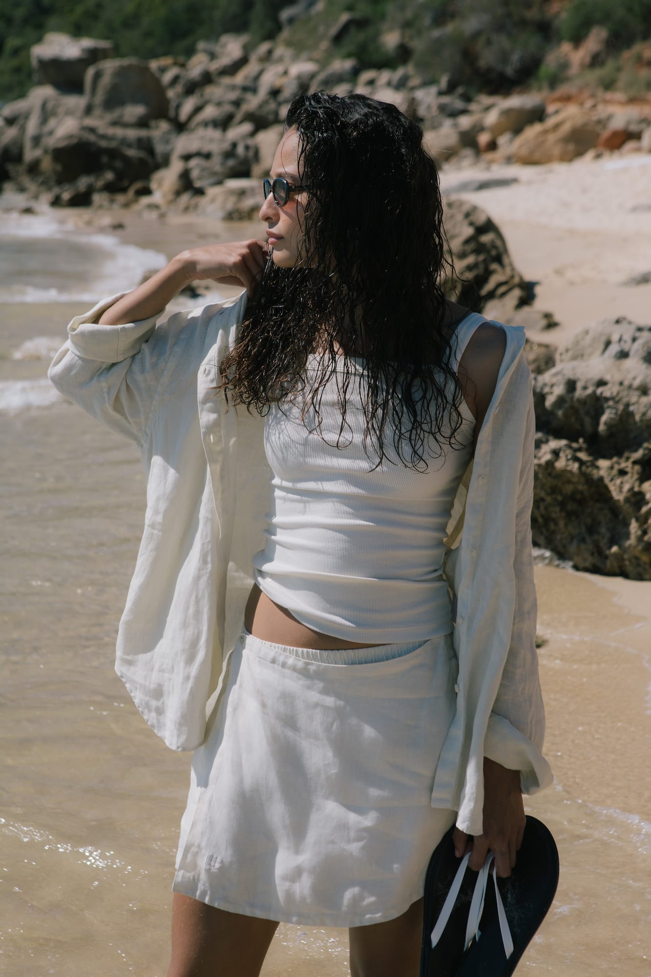 Off-white oversized linen button-down shirt, white ribbed tank, linen mini skirt worn by woman on beach
