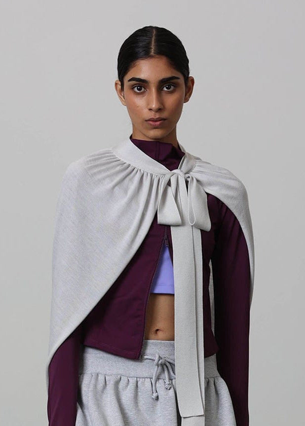 Elegant woman in heather grey gathered tie-front cape, deep plum mock-neck top, and grey loungewear joggers. Premium knit design