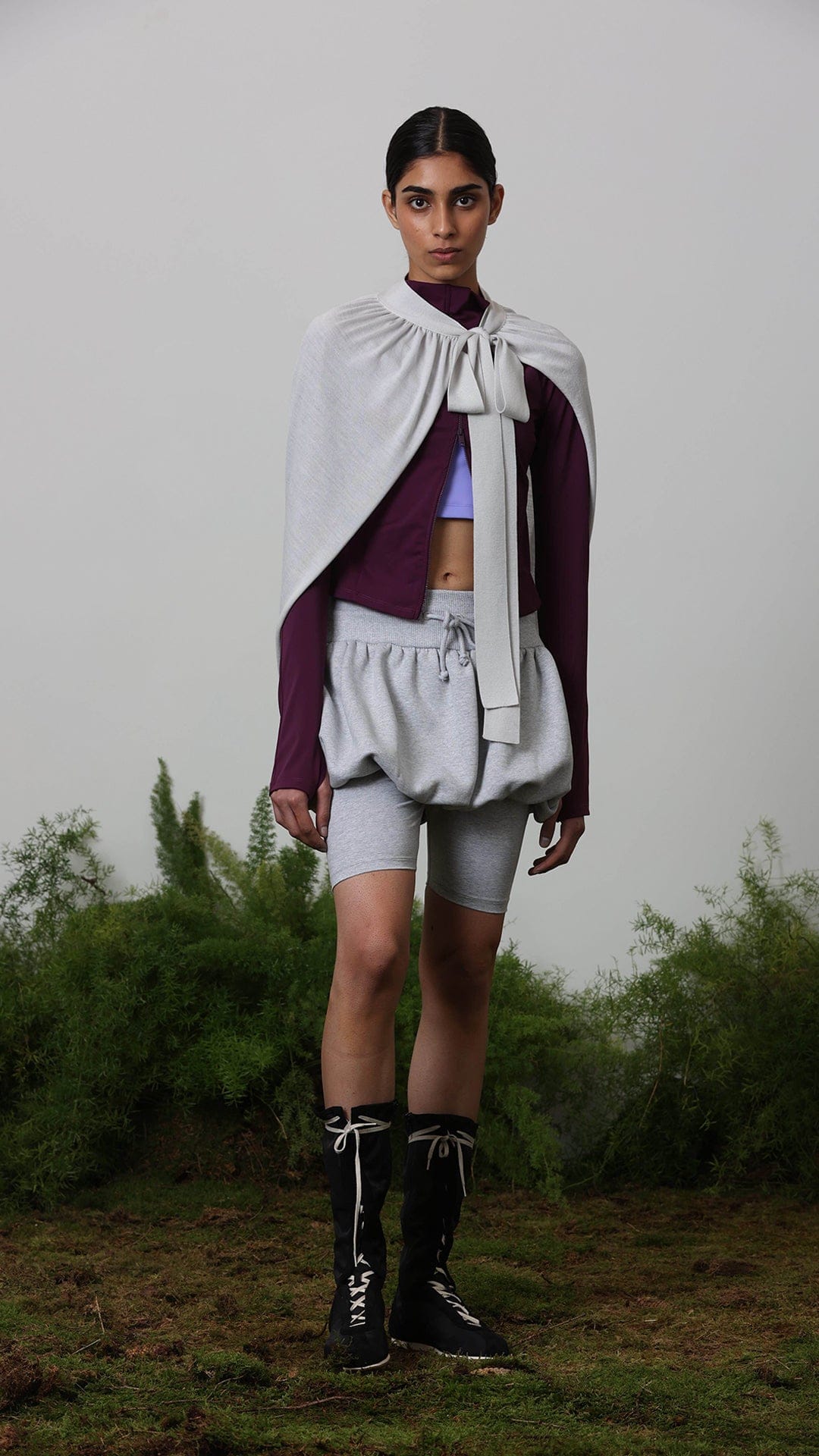 Grey bow-tie cape, plum long-sleeve zip top, lavender bra, grey bloomer shorts over biker shorts, black lace-up boots