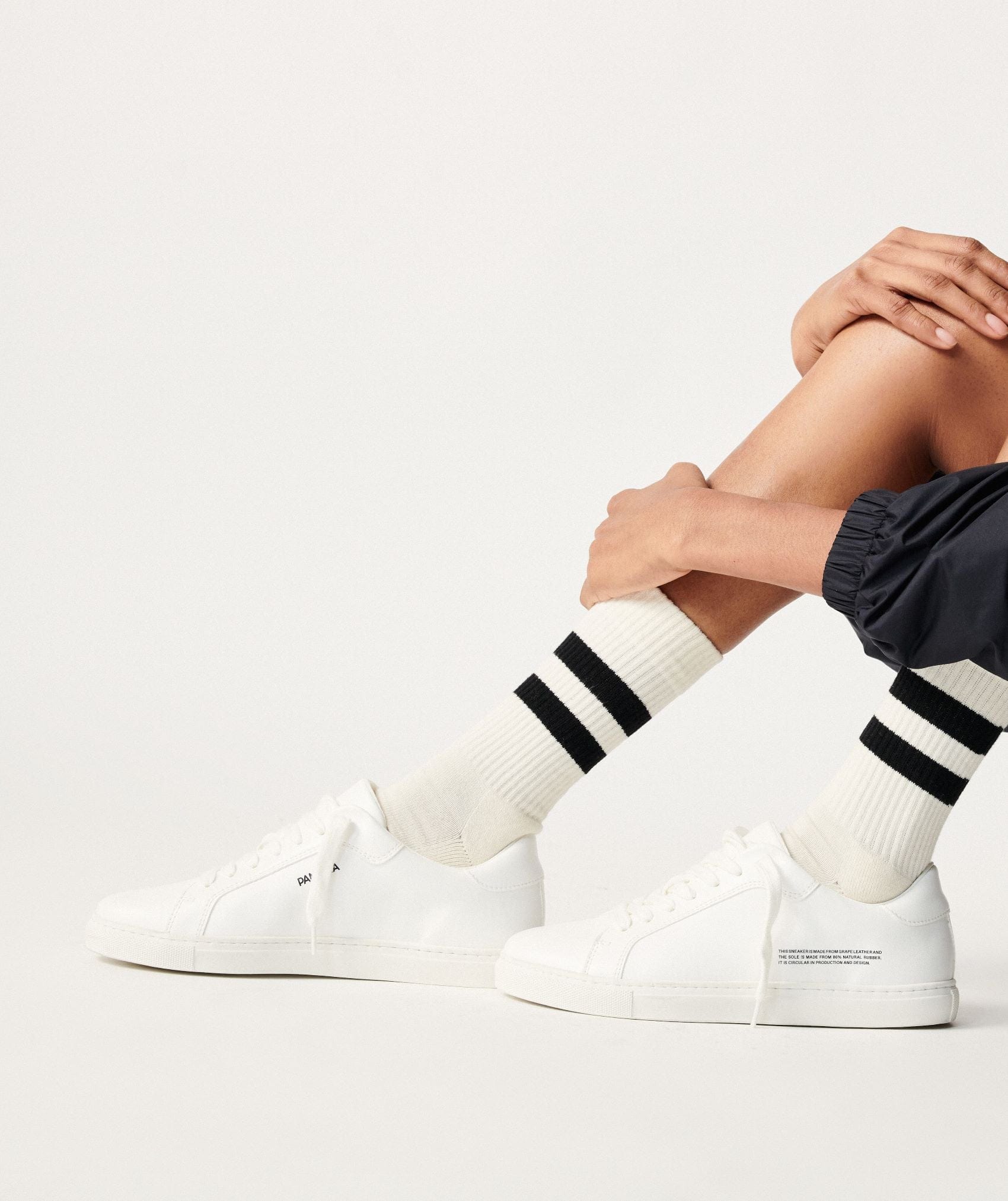 White grapeleather low-top sneakers with cream ribbed crew socks and dual black stripes on model's legs
