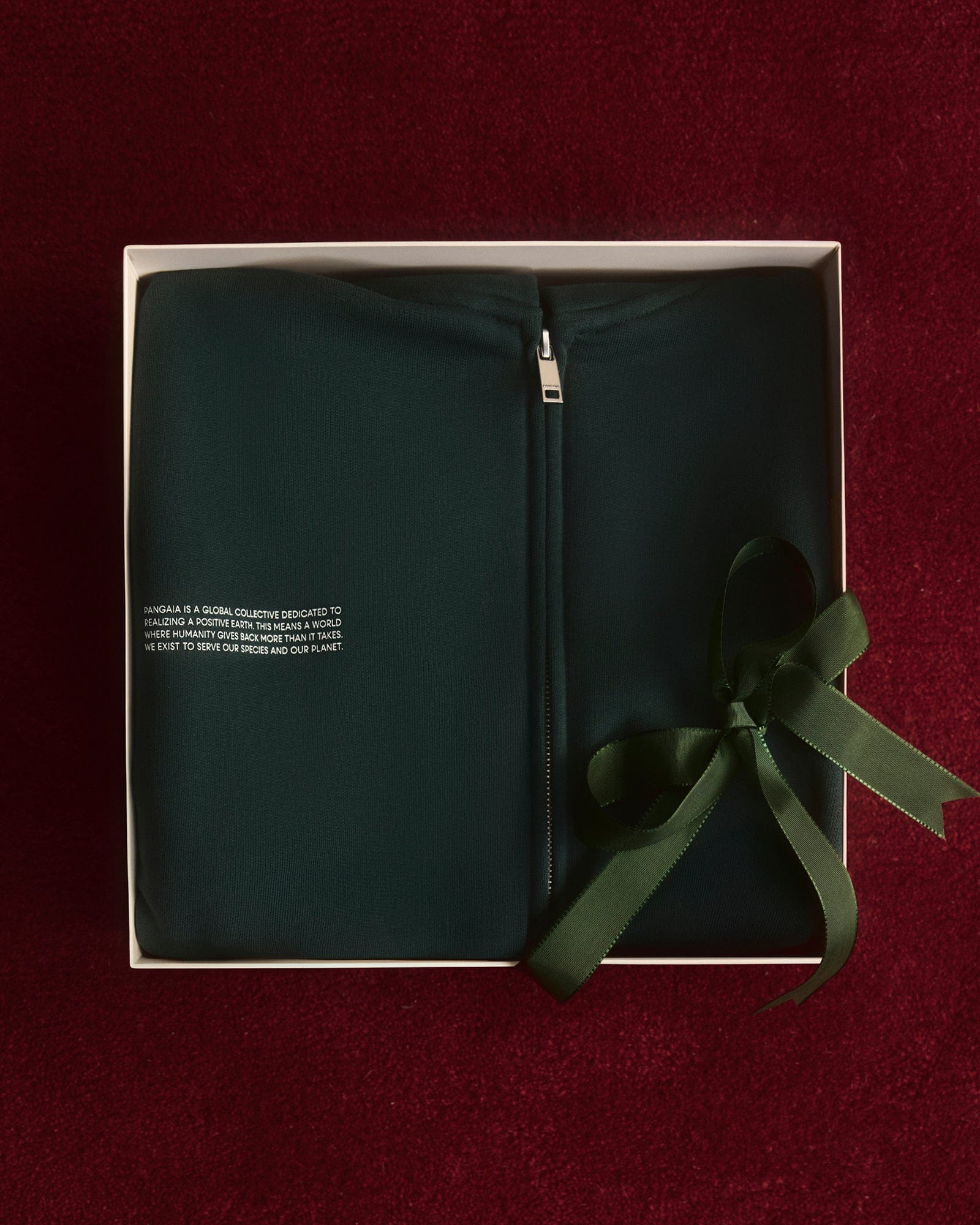 Dark green full-zip sweatshirt packshot, folded in white gift box with deep green satin ribbon. Premium knit, silver metal zipper