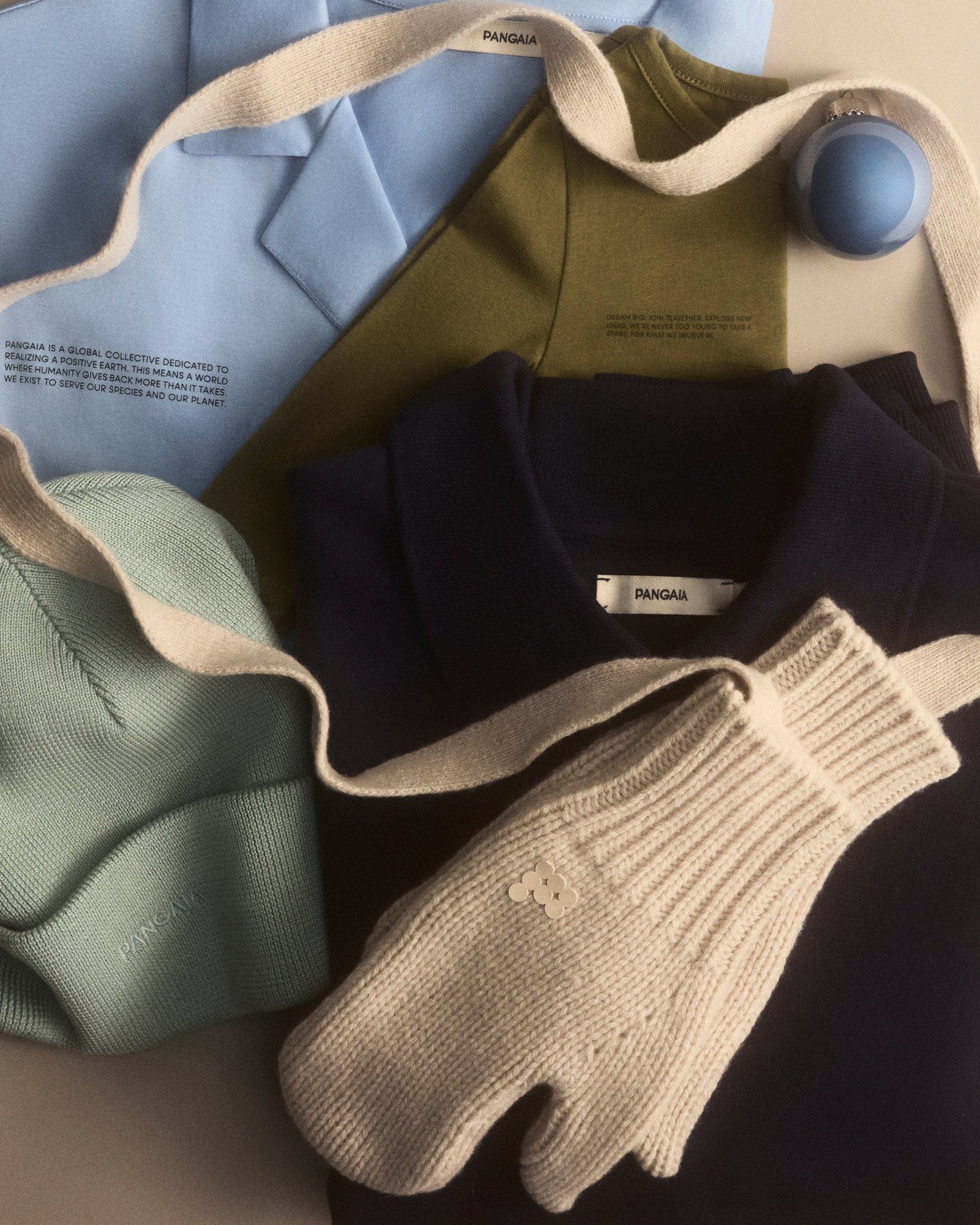 Pangaia garment packshot. Sky blue structured jacket, olive long-sleeve tee, navy fleece sweatshirt, mint knit beanie, cream chunky knit mittens